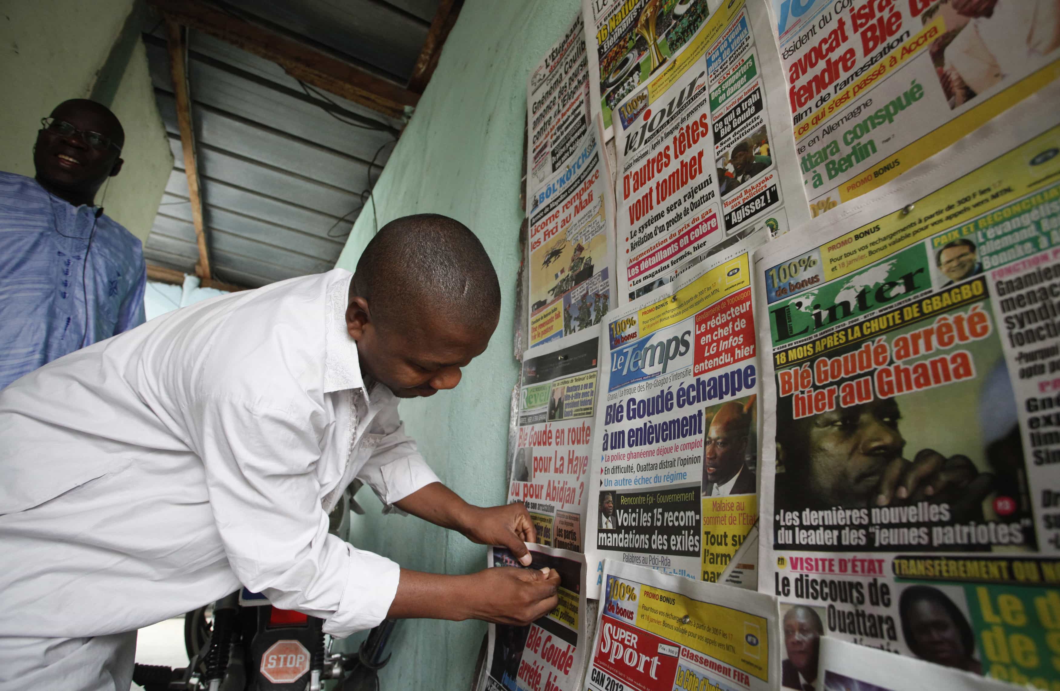 A man pins the front pages of newspapers on a wall, in Abidjan, 18 January 2013, REUTERS/Thierry Gouegnon